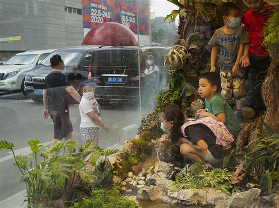 5月30日，小朋友们在北京798艺术区内游玩，一面玻璃之隔，划分出虚拟和现实的世界。 侯宇/中新社 图